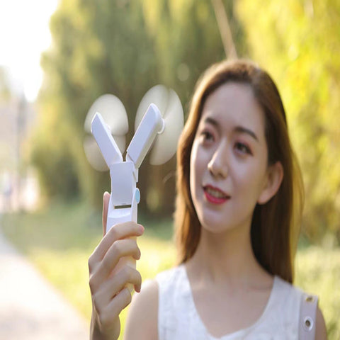 a lady holding a portable mini fan color white facing on her face to cool her body